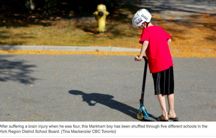 picture of a boy in a red t-shirt and black shorts with a scooter on the street, wearing a white helmet